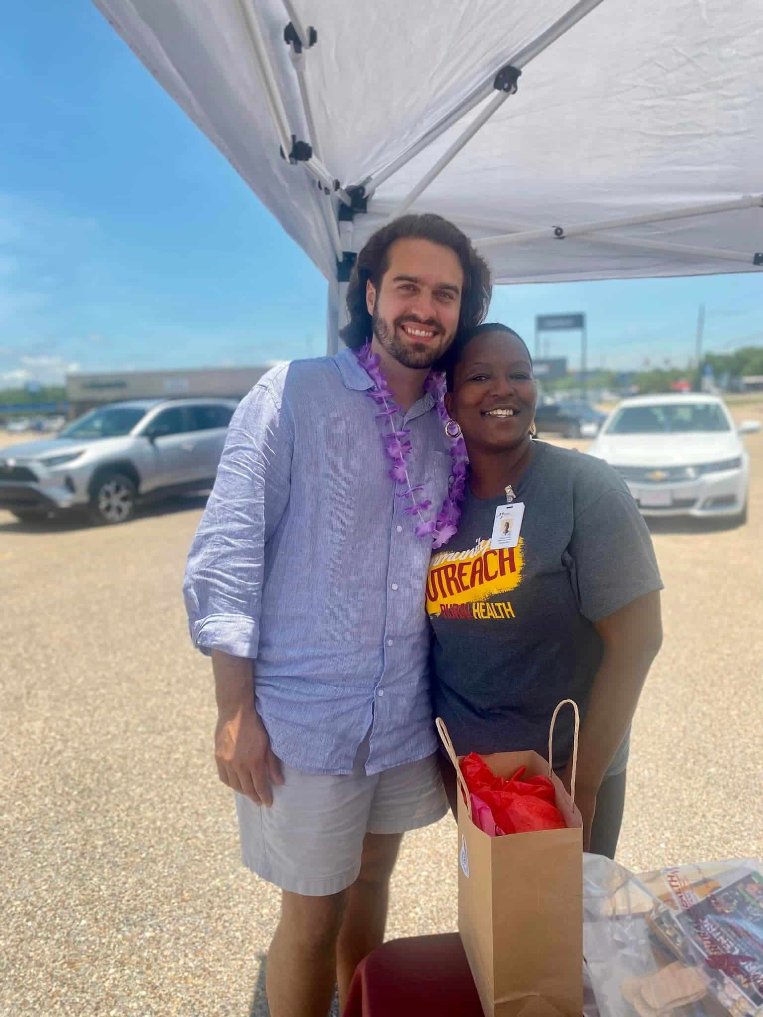 Man is hugging a woman under a tent and smiling for the camera at the ALCC Selma vendor booth